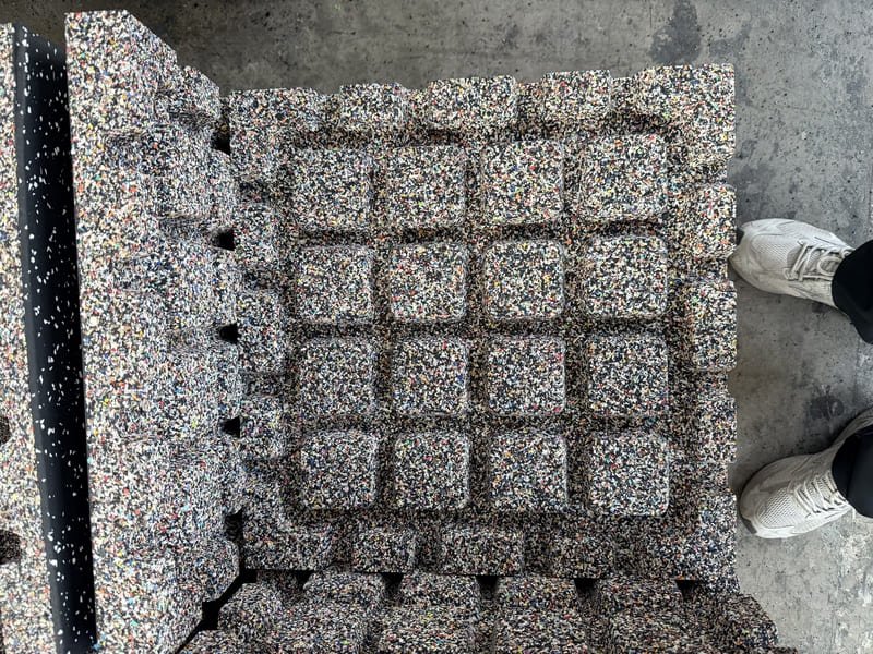 Technician inspecting white salt residue on black recycled rubber gym mats